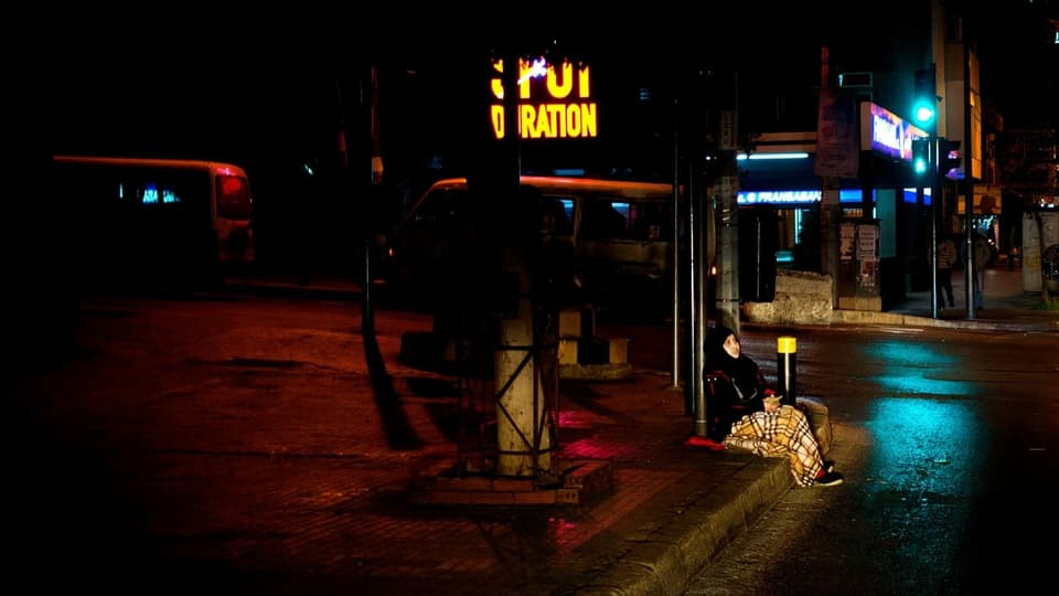 Obdachlose Frau in der Dunkelheit, sie sitzt am Strassenrand.