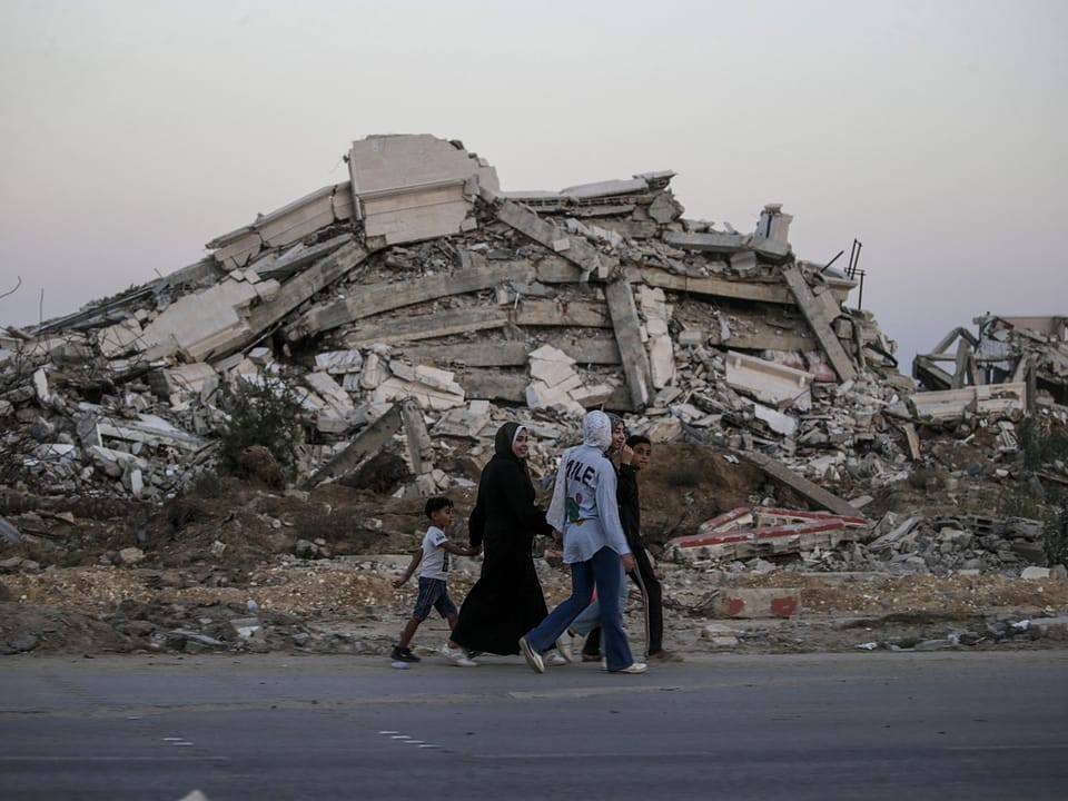 Eine Familie geht an zerstörten Gebäuden vorbei.