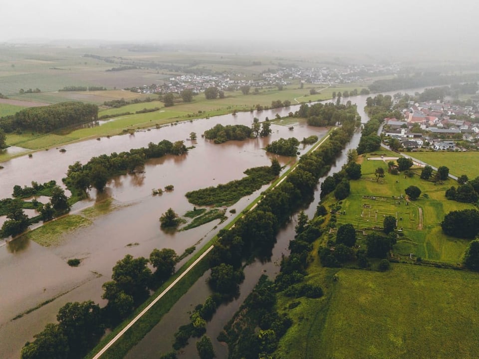 Luftaufnahme von überschwemmten Feldern und Bäumen in der Nähe eines Dorfes.