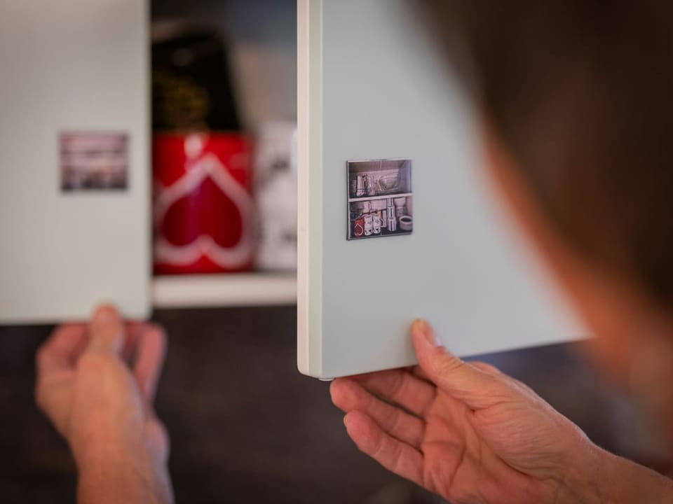 Person öffnet Küchenschrank mit kleinen Fotos an der Tür.