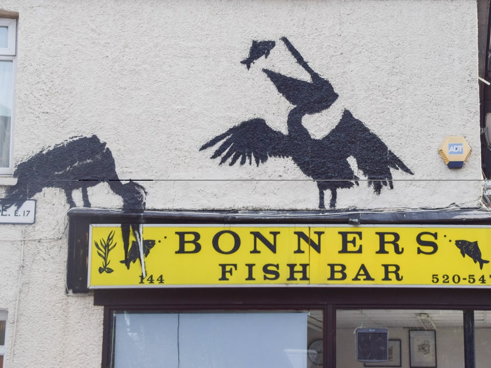 Aussenansicht eines Gebäudes mit einem gelben Schild 'Bonners Fish Bar' und schwarz gemalten Seevögeln an der Wand.