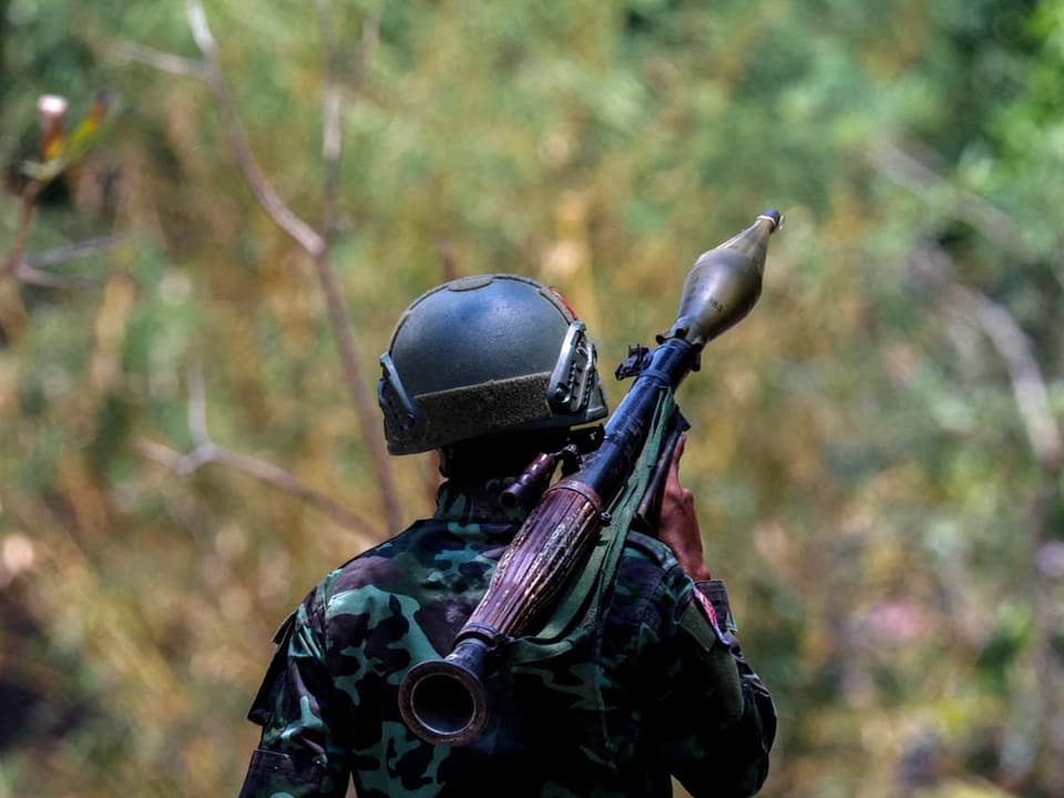 Soldat in Tarnuniform mit Gewehr und Helm steht im Wald.