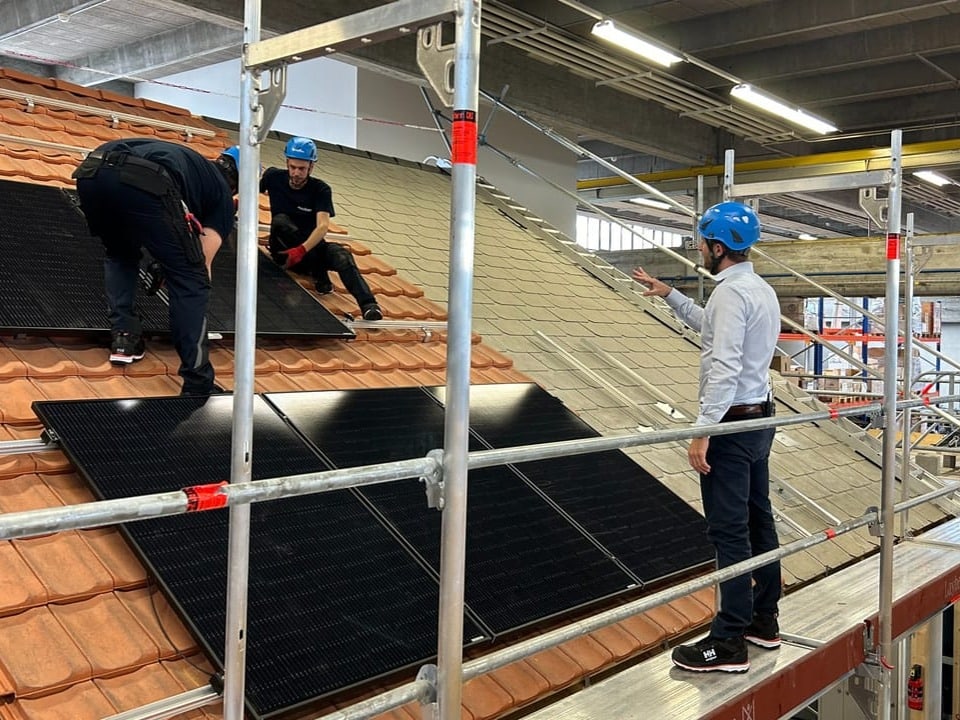 Drei Männer auf einem Dach mit Solarpanels