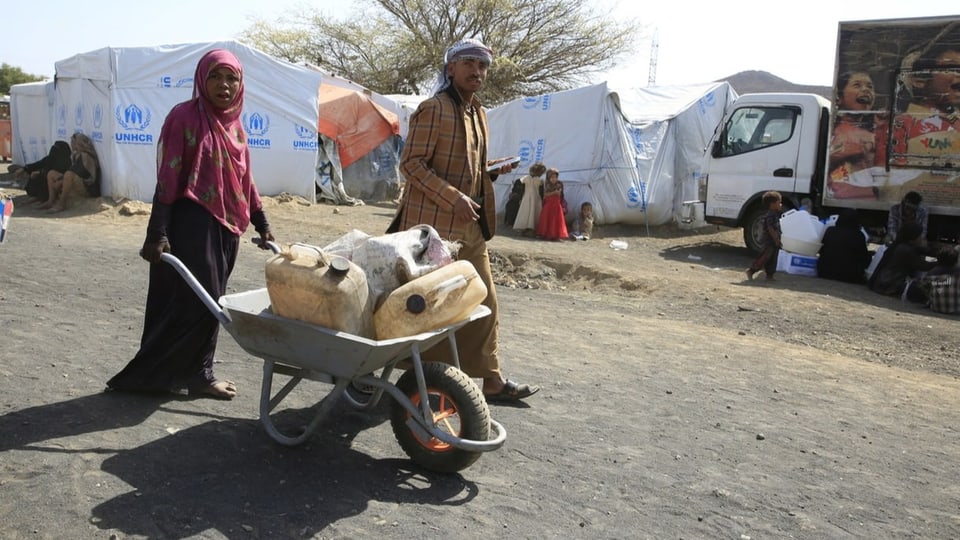Eine Frau mit einer Schubkarre mit Wasserbidons in einem Flüchtlingslager.