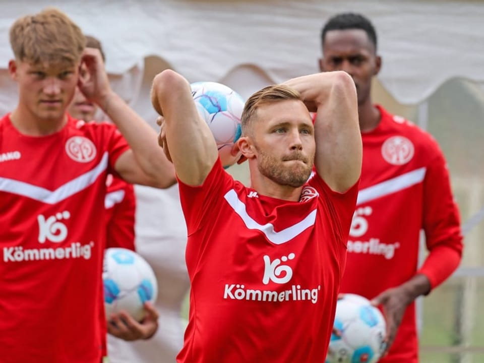 Fussballspieler im roten Trainingsanzug wirft den Ball ein.