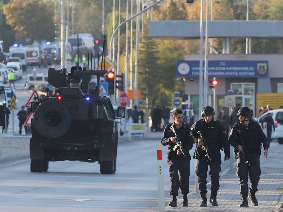 Soldaten im Vordergrund ein gepanzertes Fahrzeug im HIntergrund auf eine Strasse