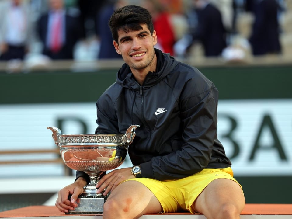 Tennisspieler sitzt auf der Bank und hält einen Pokal.