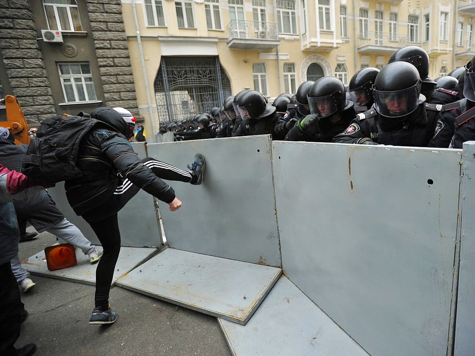 Mann tritt gegen Absperrung. Dahinter Polizisten.