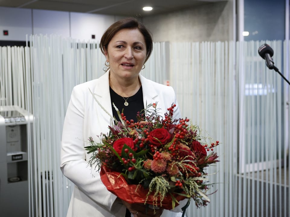 Eine Frau in weissem Blazer mit einem roten Blumenstrauss in der Hand.