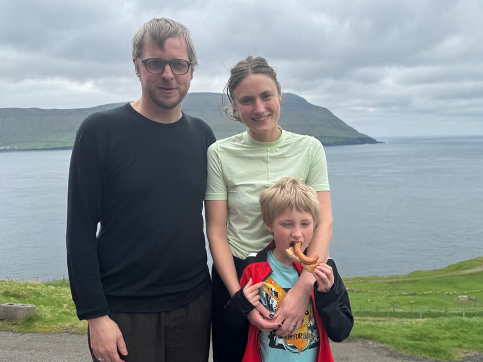 Familie posiert vor Landschaft mit Meer und Hügeln.