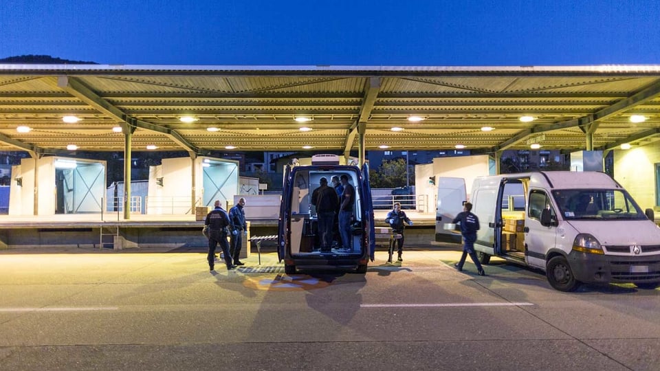 Ein Zoll: Grenzwächter entladen Sachen aus einem weissen Auto.