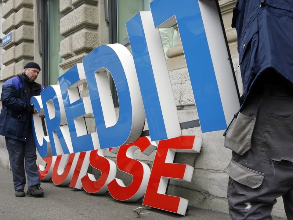 Zwei Männer halten neues (farbiges) Logo der Credit Suisse hoch.