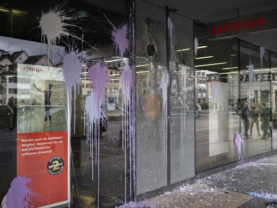 Aufnahme von Schaufenster einer Bank in Zürich. Es hat Farbflecken. Zwei Scheiben sind beschädigt.