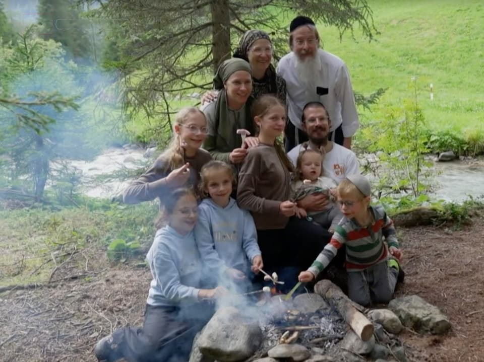 Grossfamilie posiert hinter rauchendem Lagerfeuer.