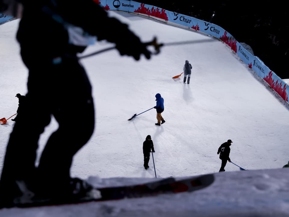 Personen räumen Schnee auf Skipiste.