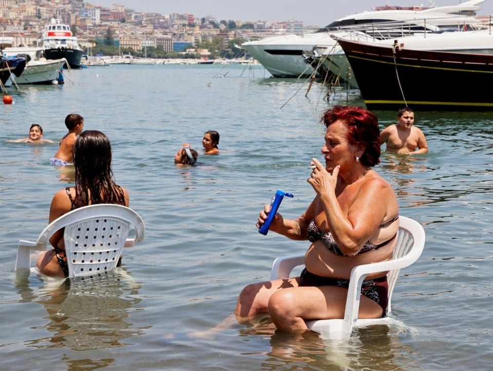 Eine Frau sitzt auf einem Plastikstuhl im Meer und raucht dabei.