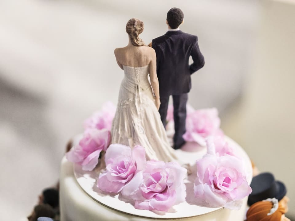 Hochzeitstortenaufsatz mit Braut und Bräutigam und rosa Blumen.