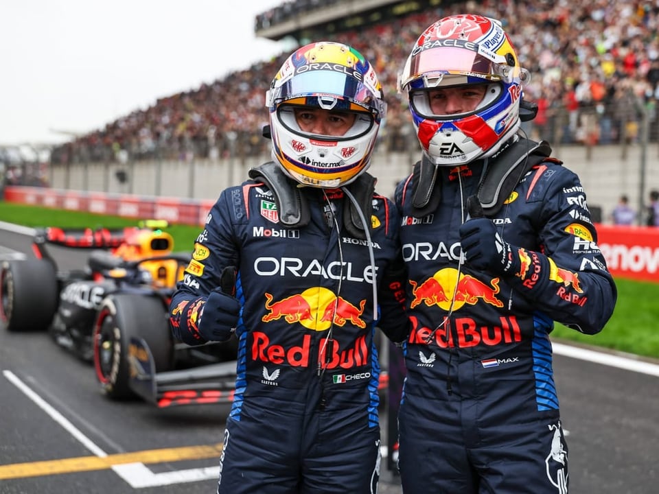 Zwei Rennfahrer in Red Bull-Anzügen auf der Rennstrecke.