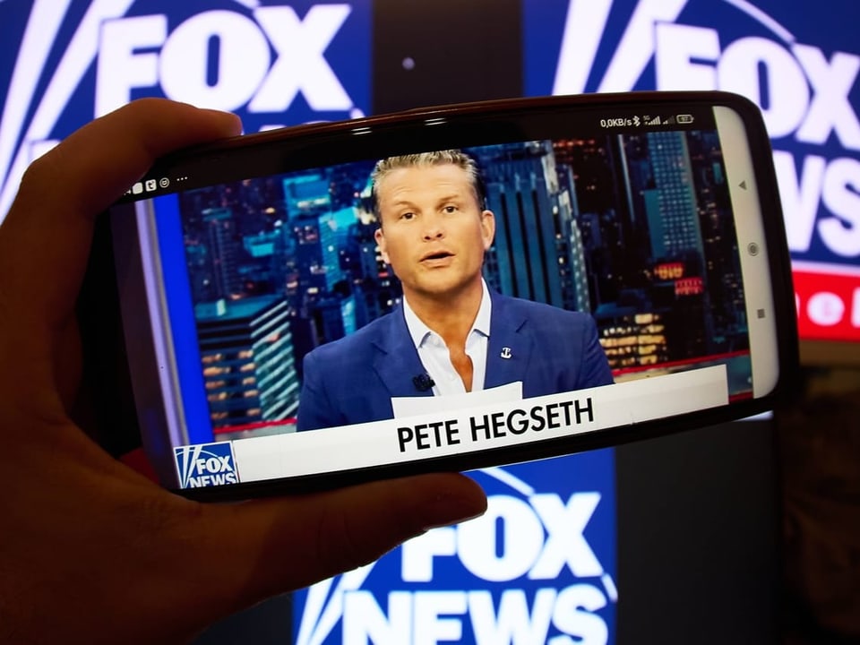 Mann auf Smartphone-Bildschirm mit Fox News im Hintergrund.