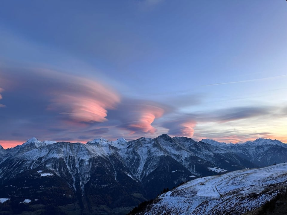 Bergpanorama mit dramatischen Wolken und Schneespitzen bei Sonnenuntergang.