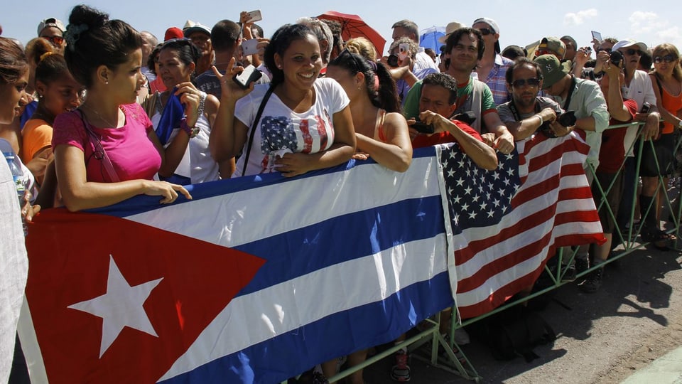 Menschen an einem Zaun mit den Flaggen der USA und Kuba.