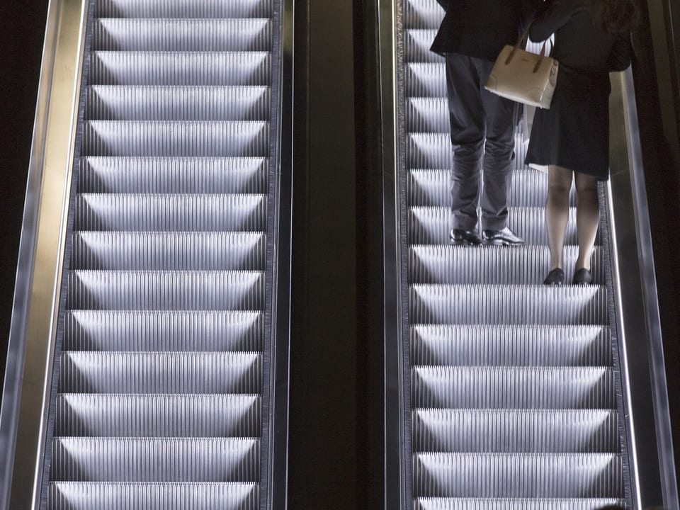 Zwei Personen auf Rolltreppe.