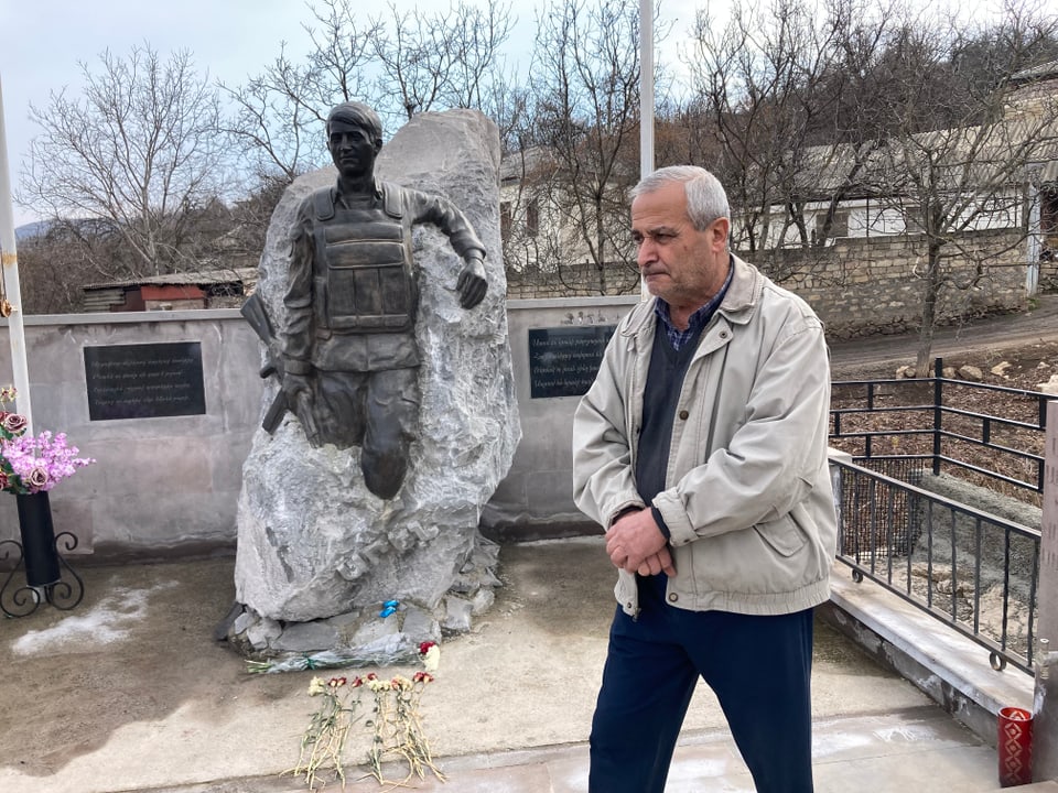 Ein Mann steht vor einem Steinbrocken, aus dem ein Soldat mit Gewehr herausragt, es ist ein Kriegsdenkmal