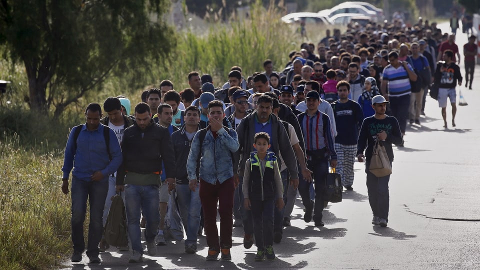 Eine lange Menschenkolonne marschiert auf einer Strasse. Es sind vorwiegend Männer.