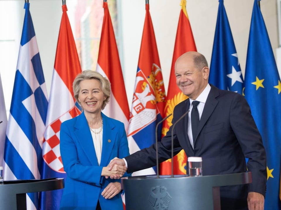 Zwei Personen schütteln sich vor nationalen Flaggen die Hand.