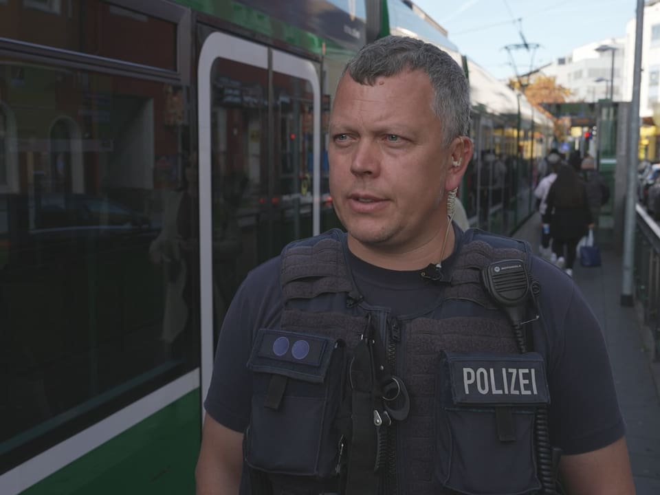 Polizist in Uniform vor grünem Zug auf einem Bahnsteig.