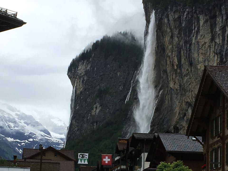 Dorf in engem Tal mit Felswänden. Von den Wänden stürzen sich Wasserfälle. 