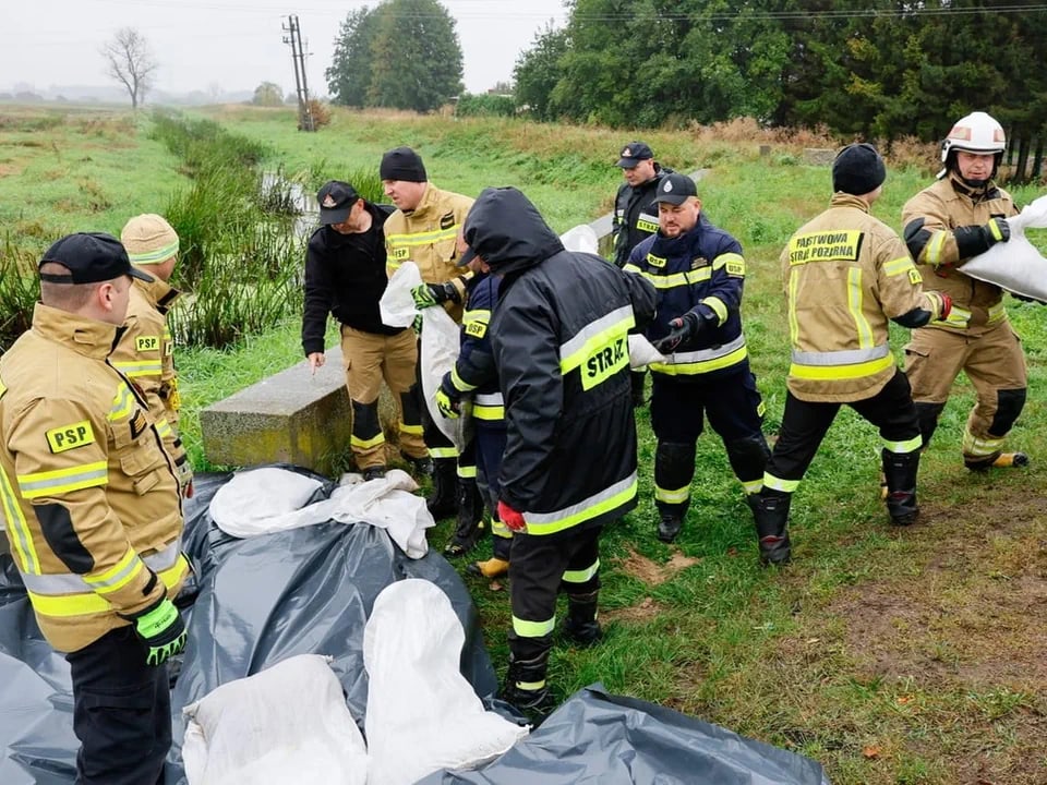 Feuerwehrleute legen Sandsäcke an einem Graben.