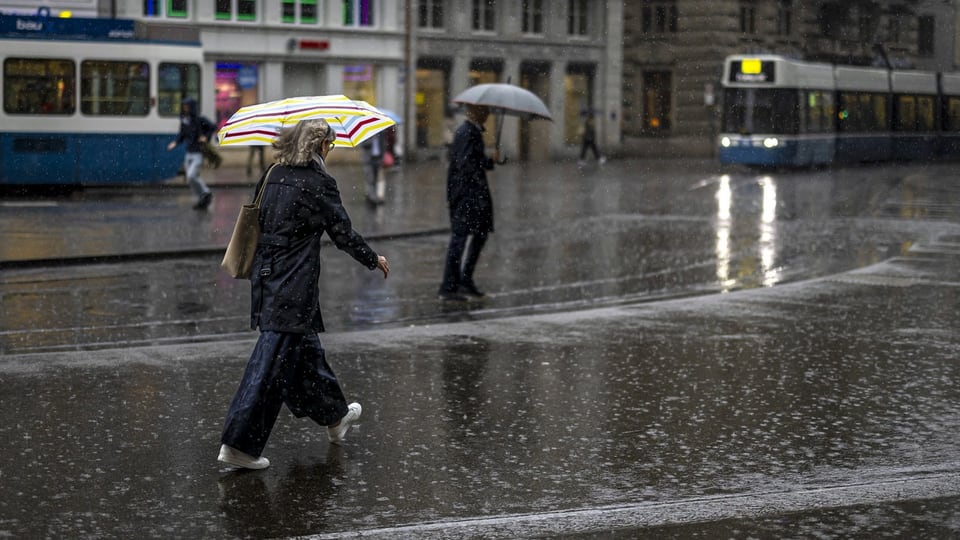 Personen mit Regenschirmen überqueren nasse Strasse bei Regen.