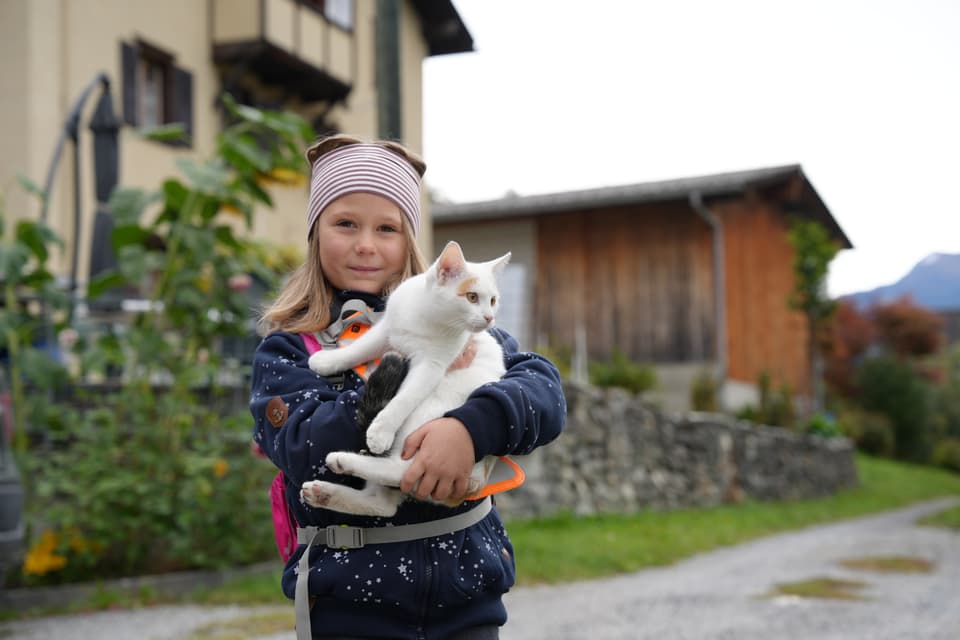 Mädchen hält weisse Katze im Freien vor einem Haus.