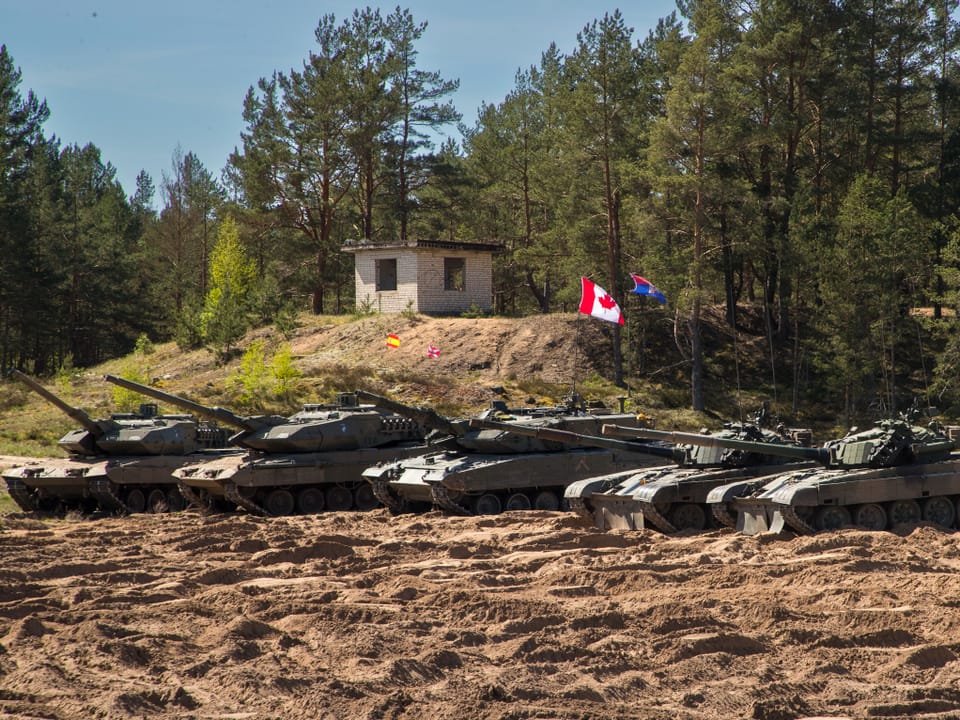 Panzer im Wald neben einem kleinen Gebäude mit kanadischer Flagge.