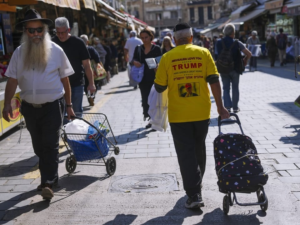 Menschen mit Einkaufstrolleys auf belebter Marktstrasse.