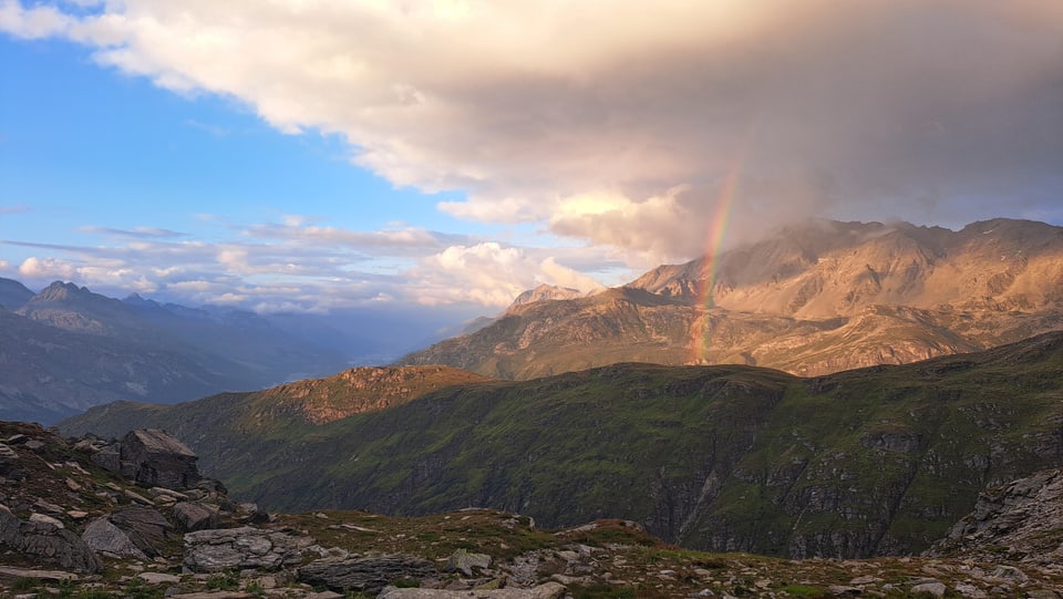 Blick auf eine Berglandschaft mit einem Regenbogen und wolkigem Himmel.