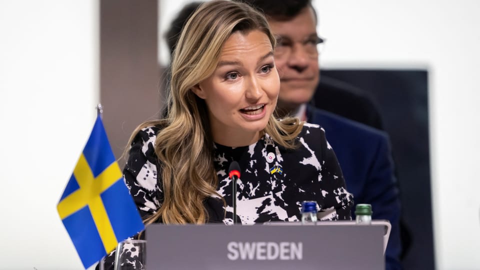 Ebba Busch spricht bei einer Veranstaltung hinter einem Rednerpult mit Schweden-Flagge.