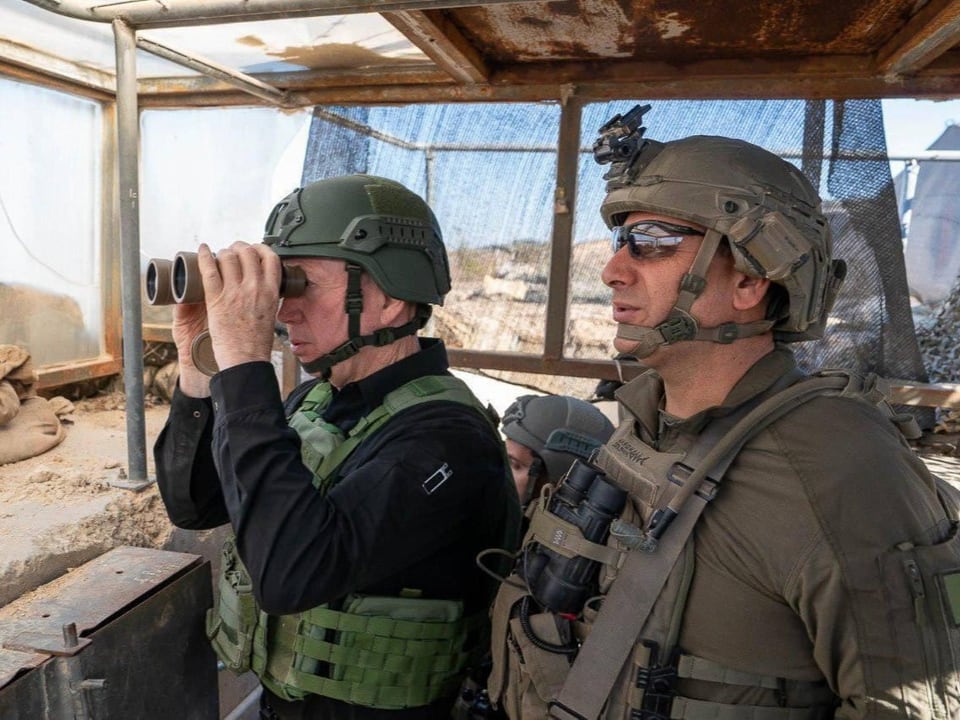 Zwei uniformierte Männer mit Fernglas in militärischer Umgebung.