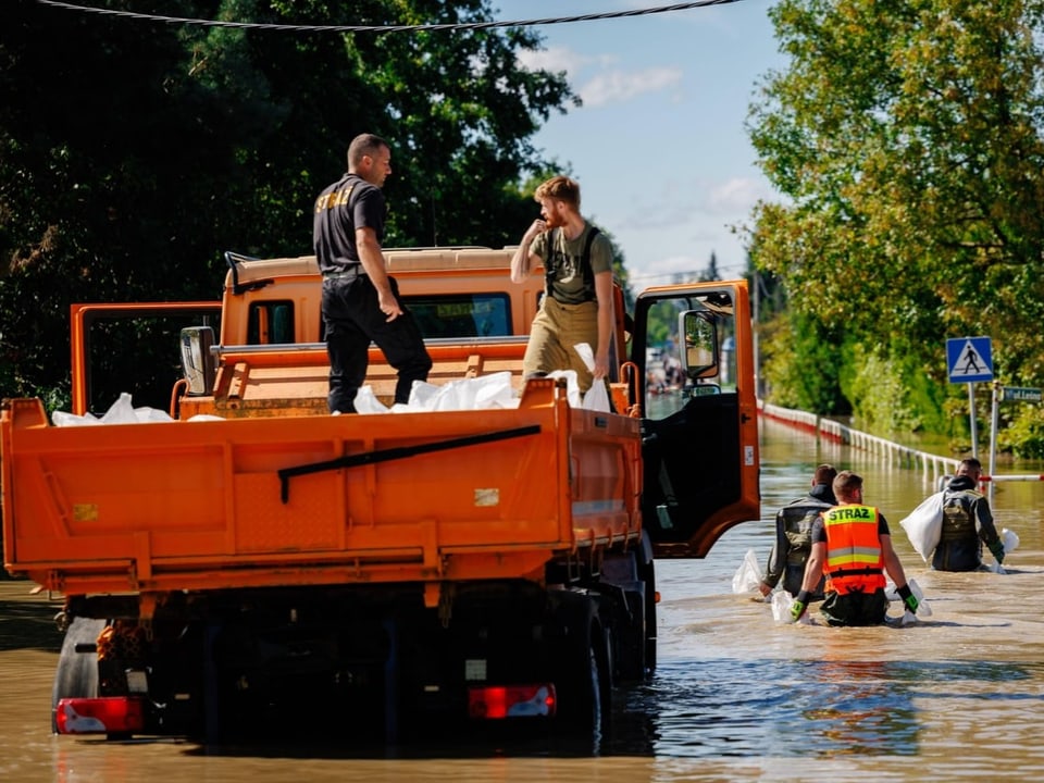 Rettungseinsatz nach Hochwasser, Menschen auf Lastwagen und im Wasser.