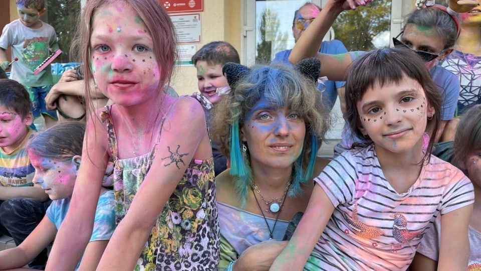 Kinder und eine Frau sind mit bunten Farben im Gesicht und an den Kleidern bemalt.