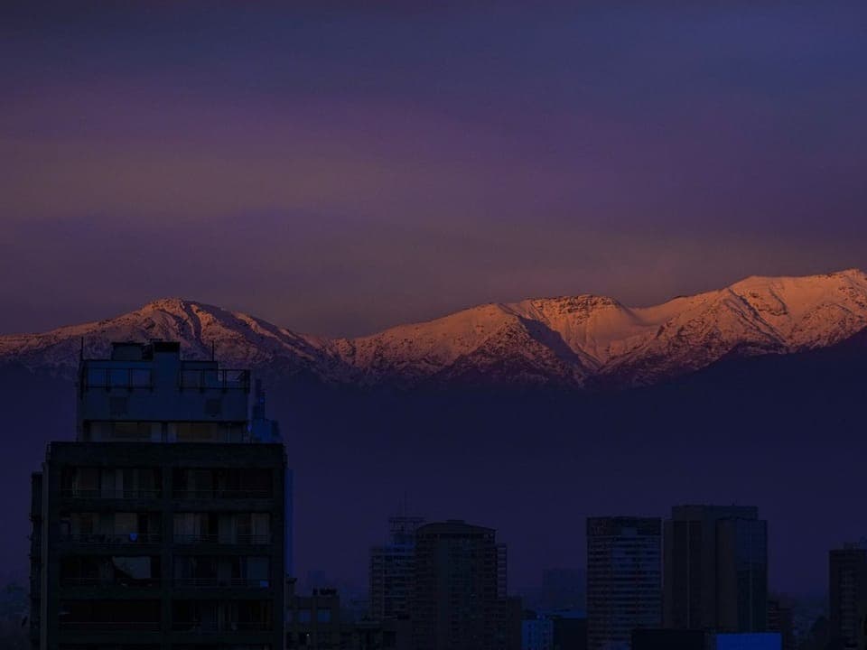 Abendlicher Blick auf schneebedeckte Berge hinter einer beleuchteten Stadt.