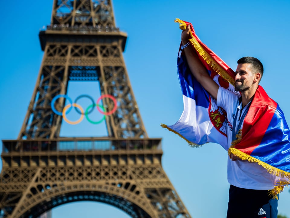 Mann mit Flagge vor Eiffelturm mit Olympischen Ringen.