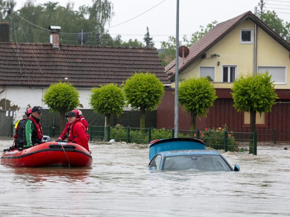 Rettungsteam auf einem Boot in einer überfluteten Wohngegend mit Auto im Wasser.