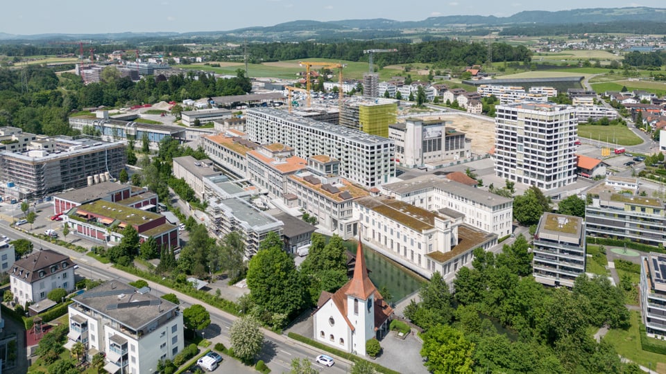 Vogelperspektive auf das Areal der ehemaligen Papierfabrik. Zwischen Neubauten stehen Kräne.