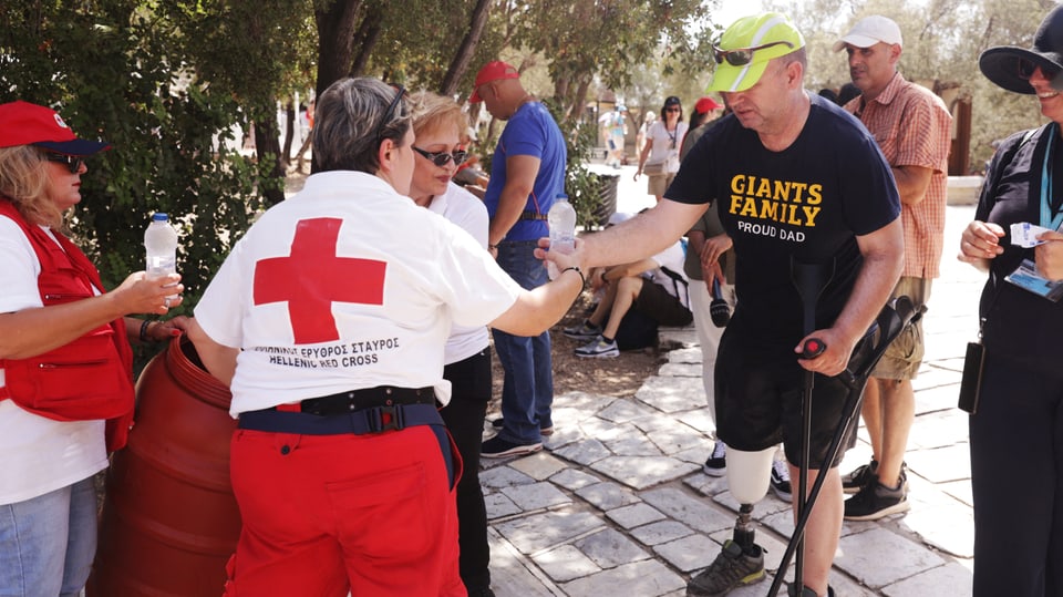 Eine Freiwillige des Griechischen Roten Kreuzes versorgt einen Touristen in der Nähe der Akropolis mit Wasser.
