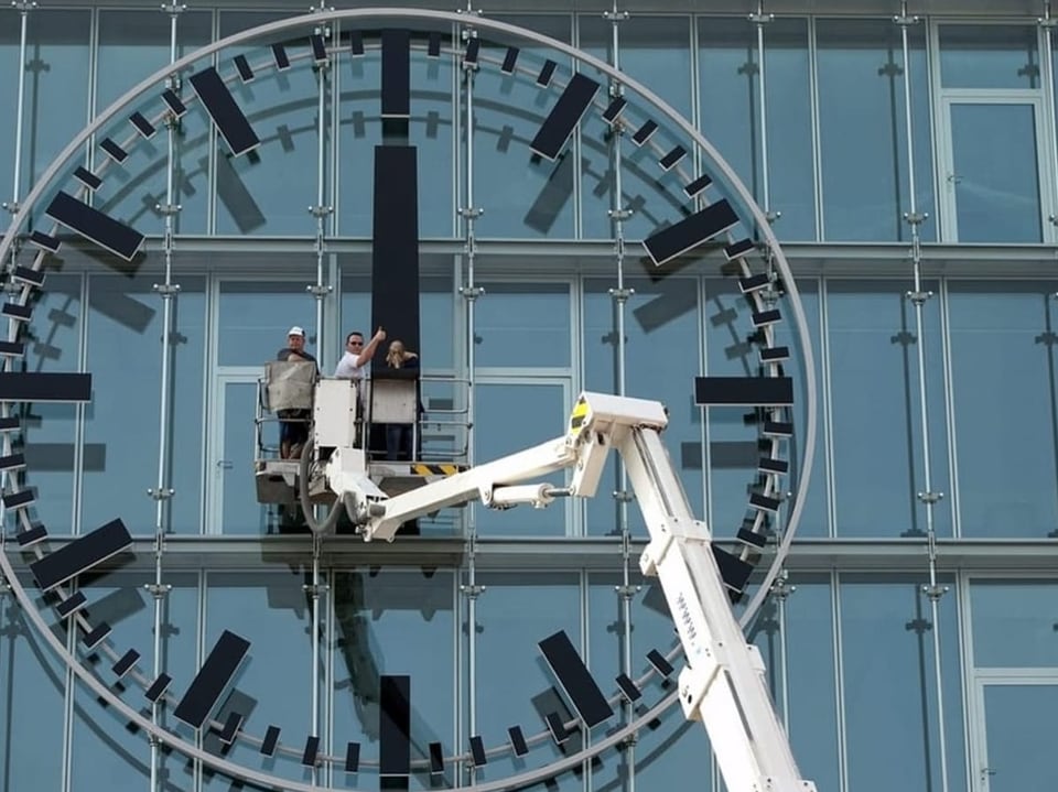 Arbeiter auf einer Hebebühne, die eine grosse Uhr an einem Gebäude reparieren.