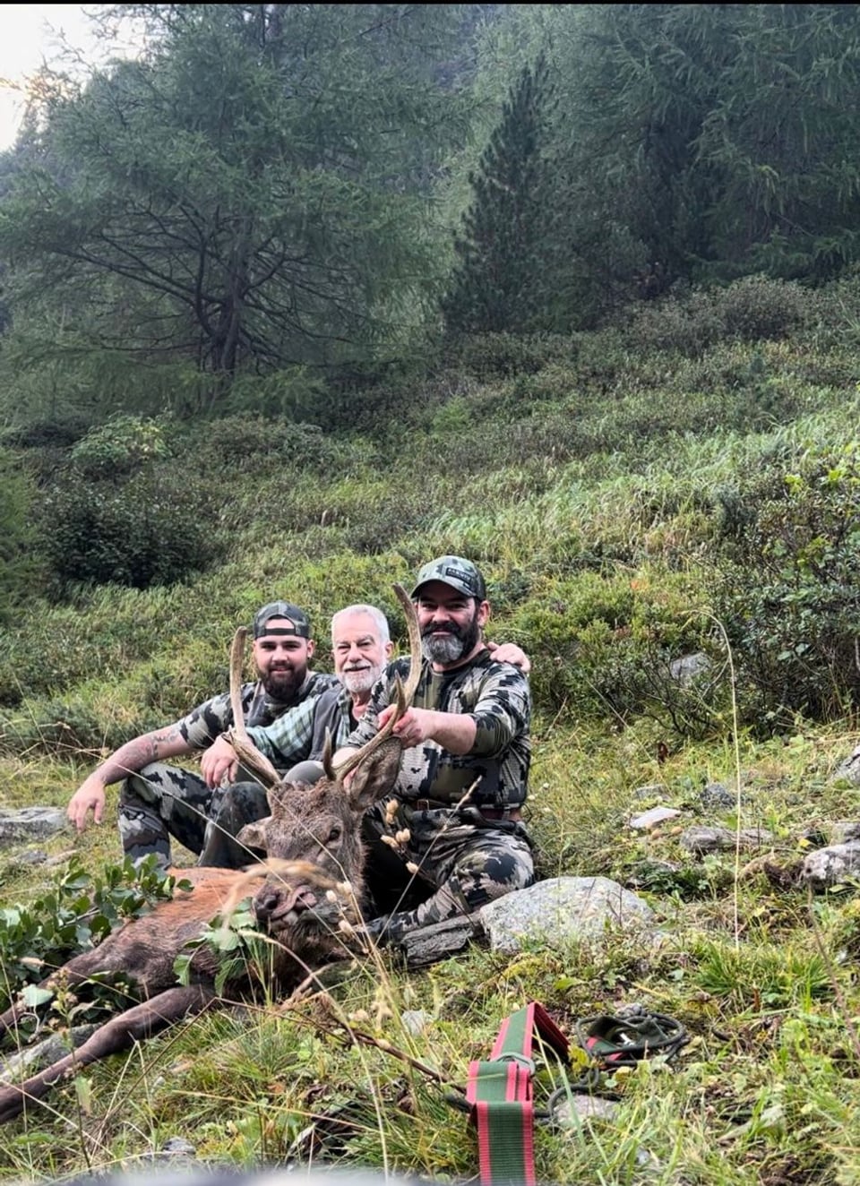 Drei Männer posieren mit erlegtem Hirsch im Wald.