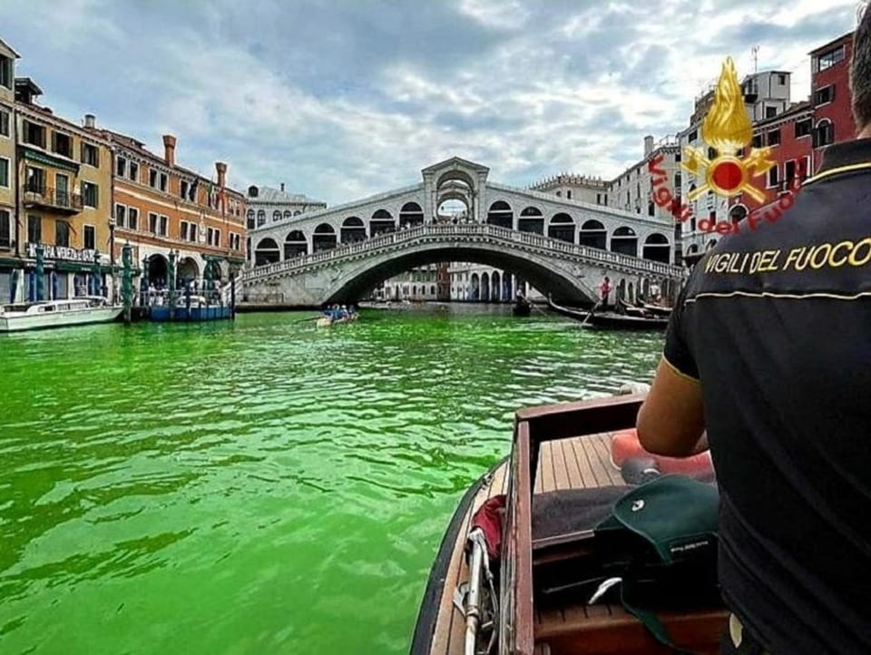 Blick auf den Canal Grande von einem Boot aus. Im Hintergrund ist die Rialto-Brücke. Der Fluss ist grün verfärbt.