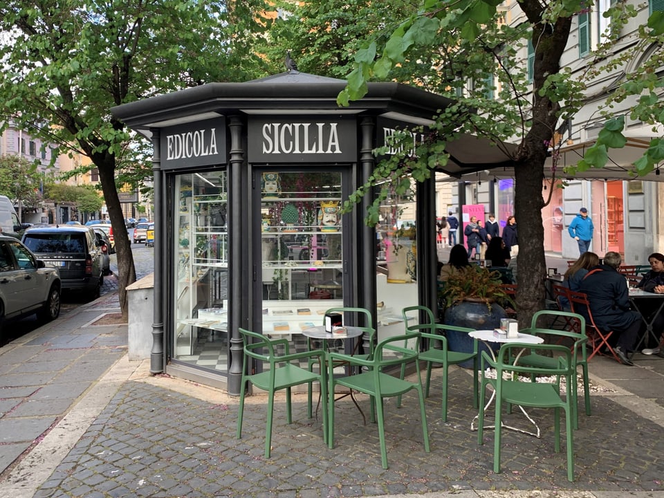Kiosk 'Edicola Sicilia' mit grünen Stühlen auf einem Gehweg in einer städtischen Gegend.